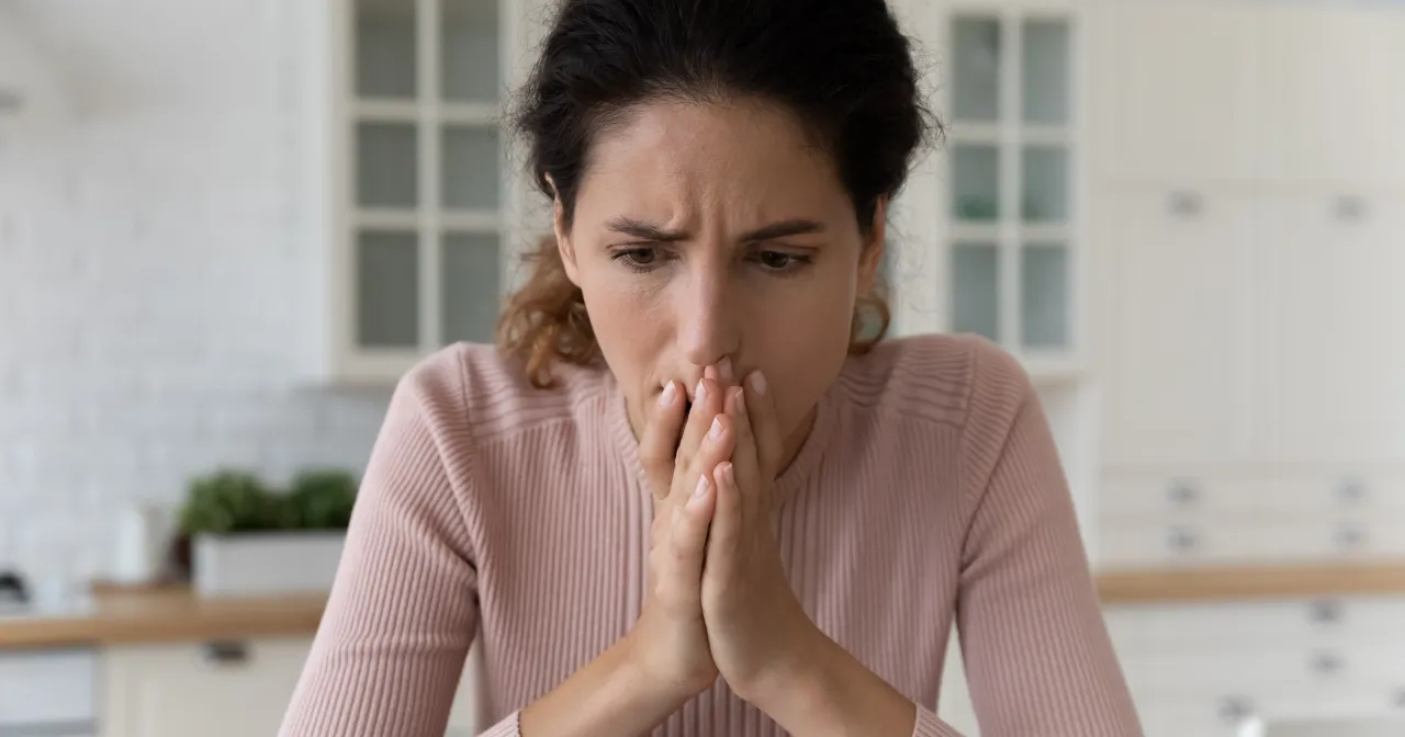 Zamyślona kobieta, z dłońmi przy ustach, odzwierciedla 24 cechy wysoko wrażliwych osób, które głęboko przeżywają emocje.