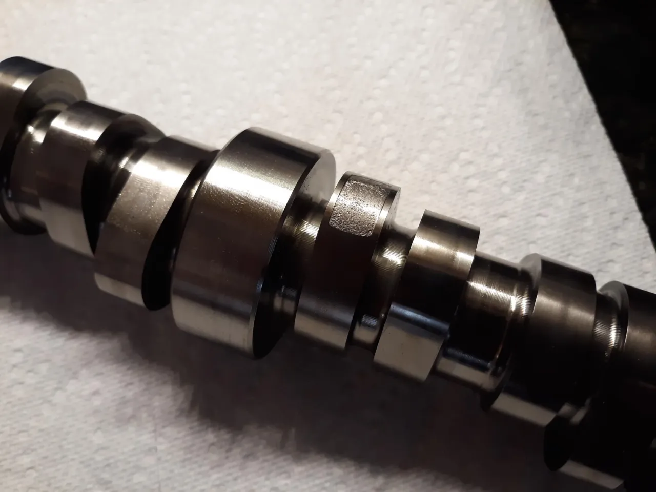 Metalowy wałek rozrządu z widocznymi śladami zużycia, wskazującymi na zużyty wałek rozrządu objawy.