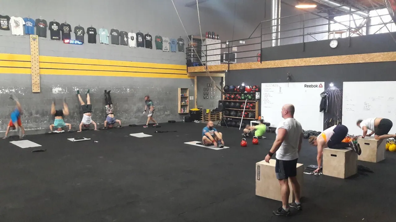Trening w stylu crossfit Warszawa, gdzie ludzie ćwiczą na rękach i wykonują inne ćwiczenia.