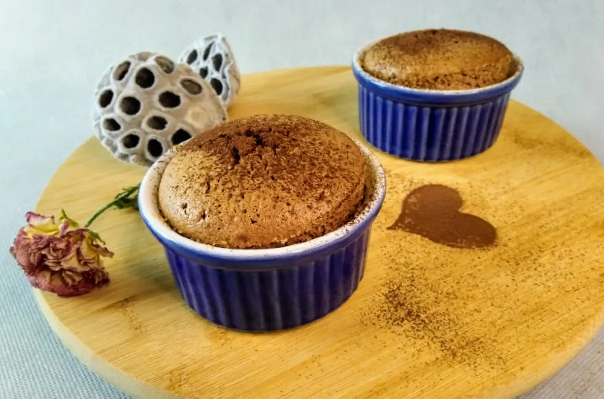 Pyszny suflet czekoladowy przepis. Dwa puchate suflety w niebieskich naczynkach, posypane kakao. Serce z kakao na desce.