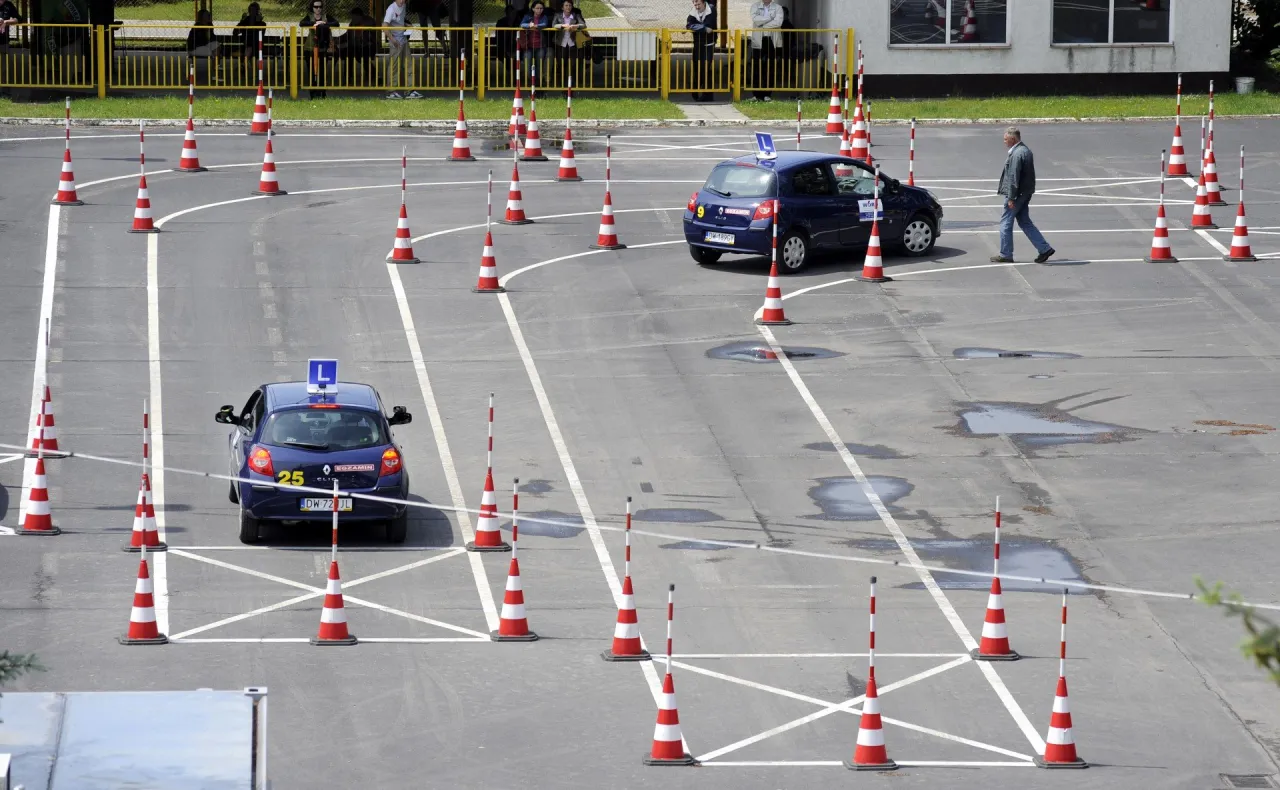 Tor przeszk&oacute;d na placu manewrowym, gdzie kursanci uczą się, jak zdać egzamin na prawo jazdy. Dwa samochody z literą 