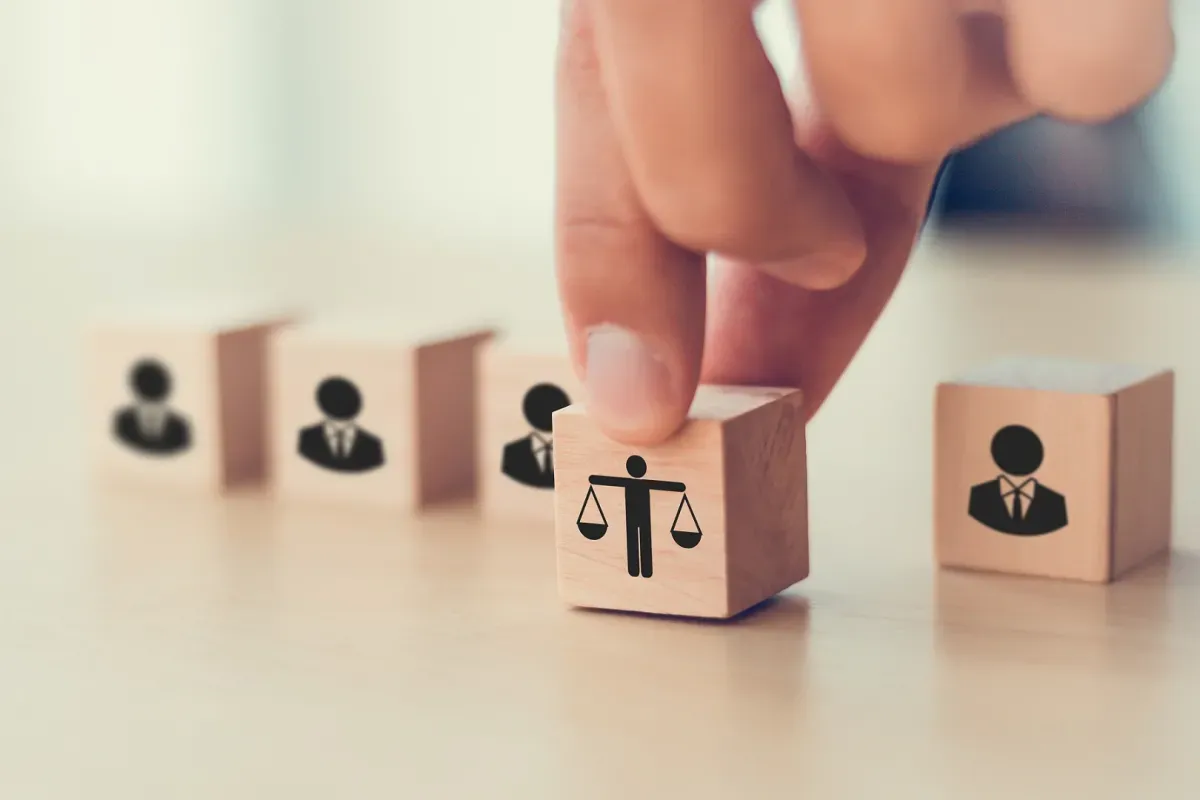 Dłoń układa kostkę z wagą sprawiedliwości obok kostek z ludzikami. To symbol tego, co daje członkostwo w partii: równość i reprezentację.