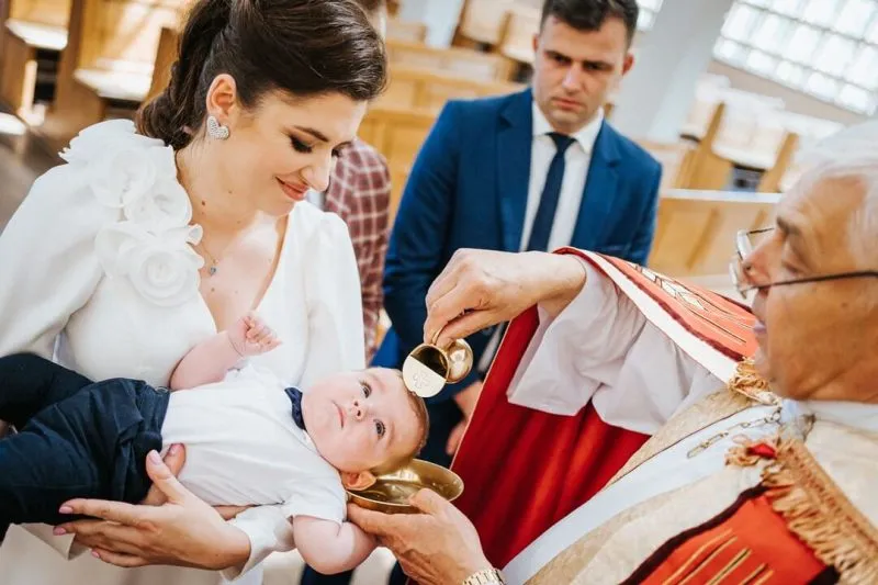 Dziecko z rodzicami chrzestnymi lub dziadkami na tle kościoła