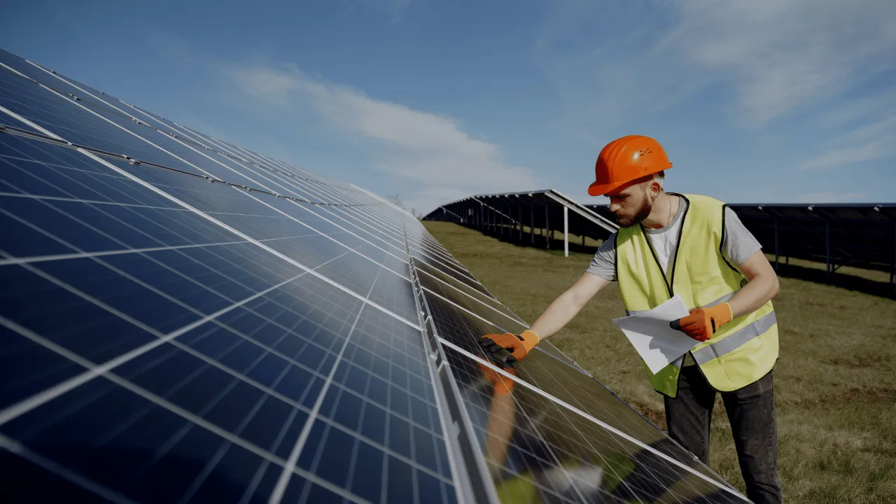 Pracownik w kamizelce i kasku sprawdza panele słoneczne. Inwestycja w OZE, wspierana przez kpo dotacje, to przyszłość.