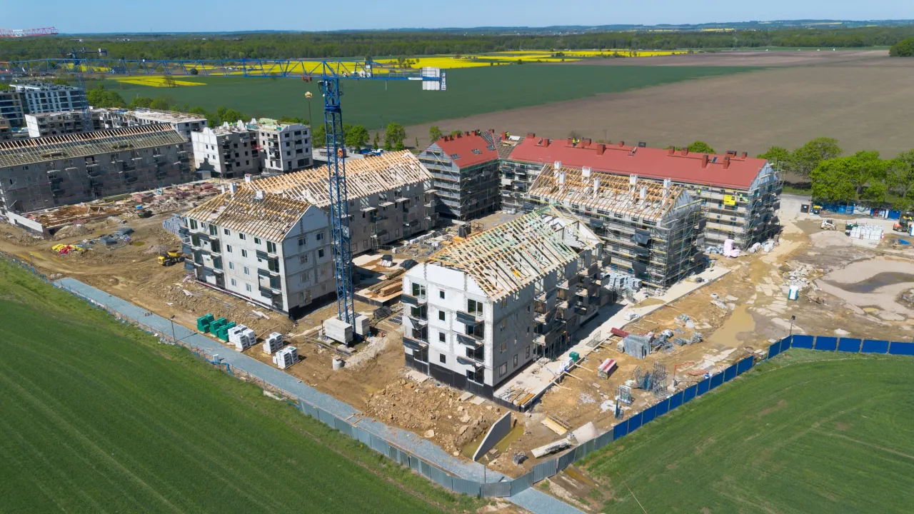 Budowa osiedla mieszkaniowego, widok z lotu ptaka. Dźwig budowlany i niedokończone budynki. Jak zacząć budowę?