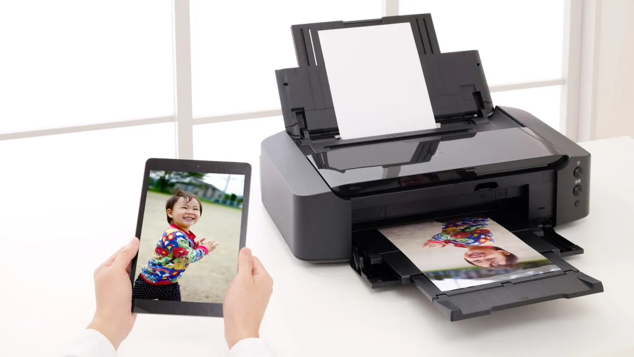Jak wywołać zdjęcia z telefonu u fotografa? Tablet z uśmiechniętym dzieckiem obok drukarki, która właśnie drukuje jego zdjęcie.