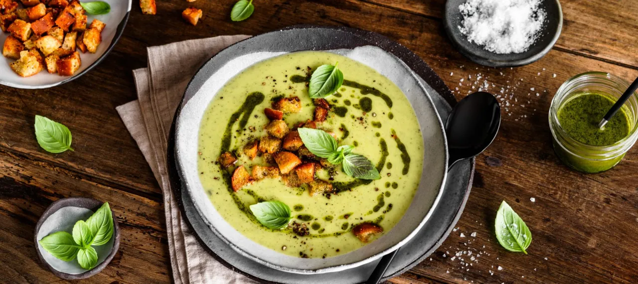 cremige Zucchinisuppe in einer Sch&uuml;ssel mit frischen Kr&auml;utern und einem L&ouml;ffel