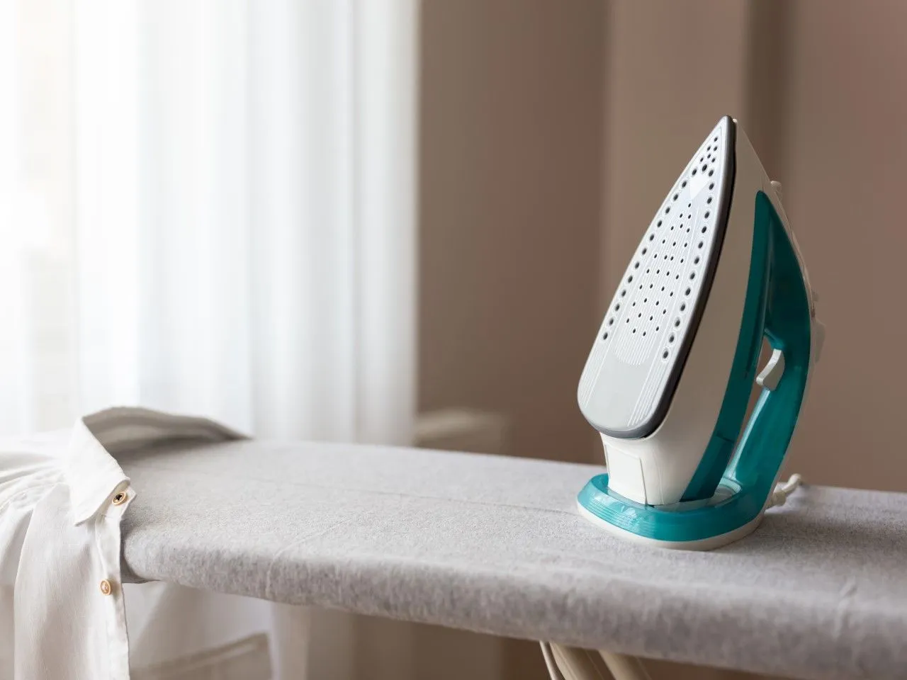 Żelazko parowe na desce, obok koszuli. Dowiedz się, jak odkamienić żelazko parowe, by prasowanie było efektywne.