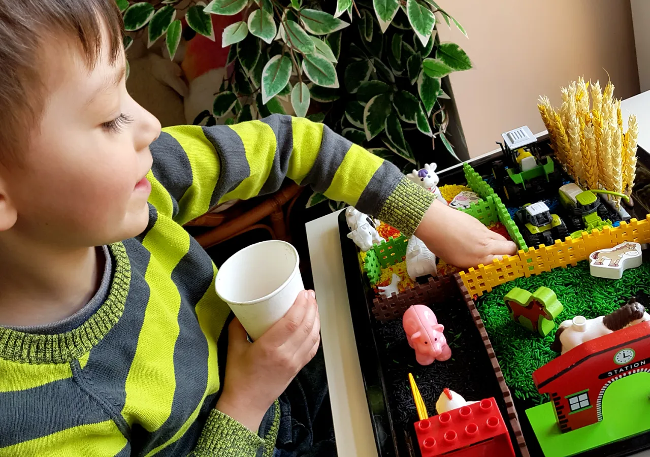 Dziecko bawi się w skrzynce sensorycznej z ryżem i zabawkami