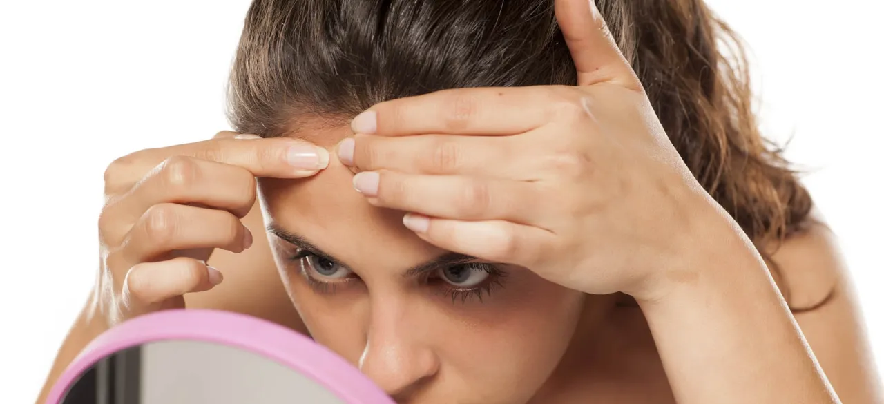 Kobieta z uwagą przygląda się swojej skórze w lusterku, zastanawiając się, kiedy wyciskać pryszcze, by nie pogorszyć stanu cery.