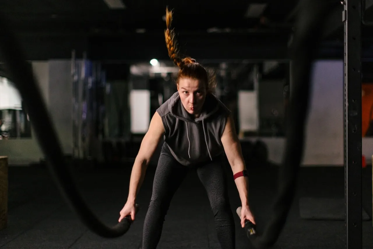 Kobieta ćwiczy z linami treningowymi, szukając sposobów, jak przyspieszyć spalanie tłuszczu. Intensywny trening w siłowni.