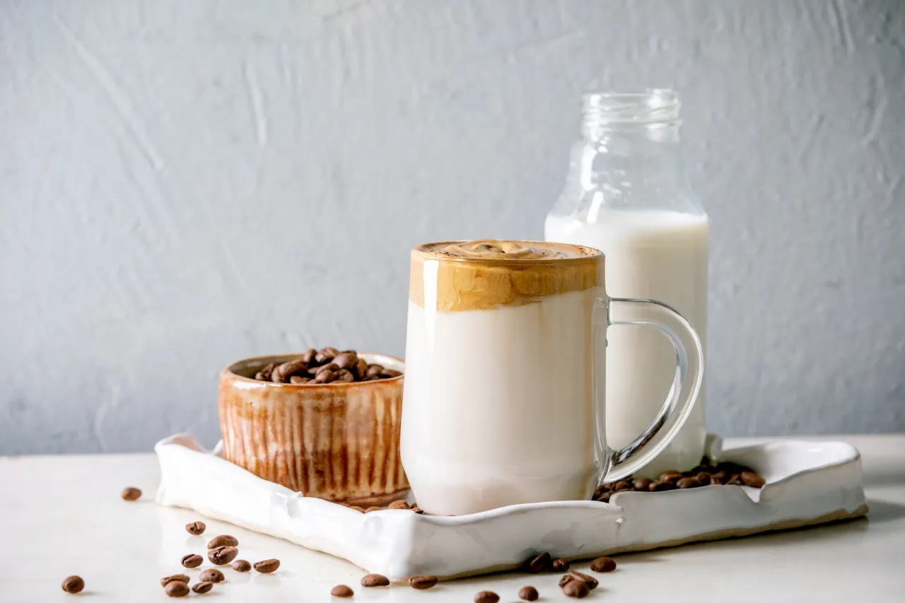 Kawa z mlekiem roślinnym, ziarna kawy i butelka mleka. Czy kawa z mlekiem roślinnym jest zdrowa?