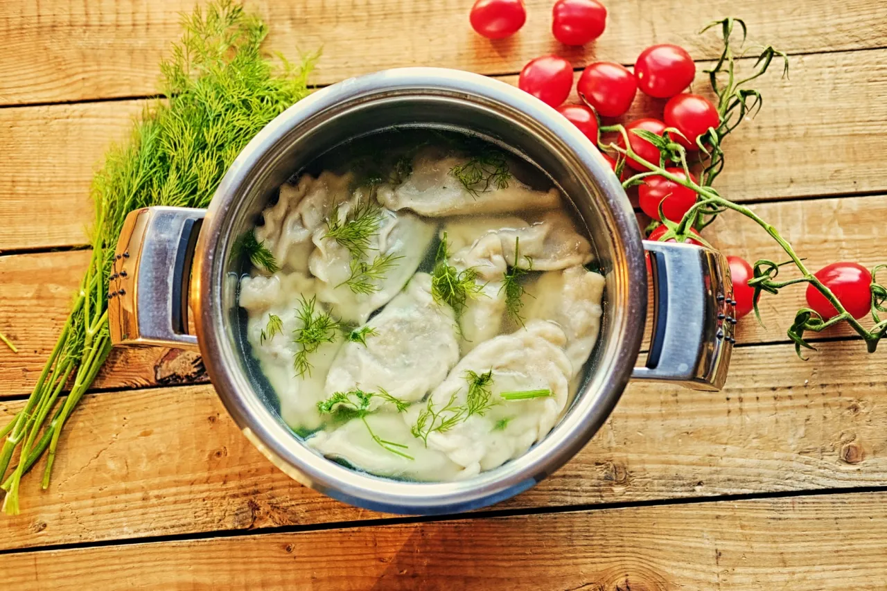 Gotujesz pierogi, by je zamrozić? W garnku pływają gotowe pierogi z koperkiem, obok pęczek koperku i pomidorki koktajlowe.