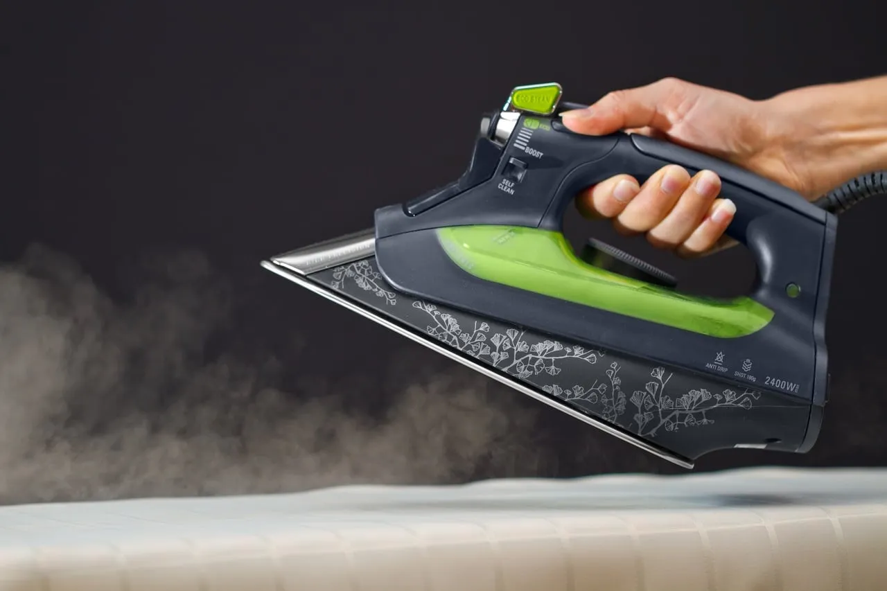 Dłoń trzyma żelazko parowe, z którego wydobywa się para. Przyciski 