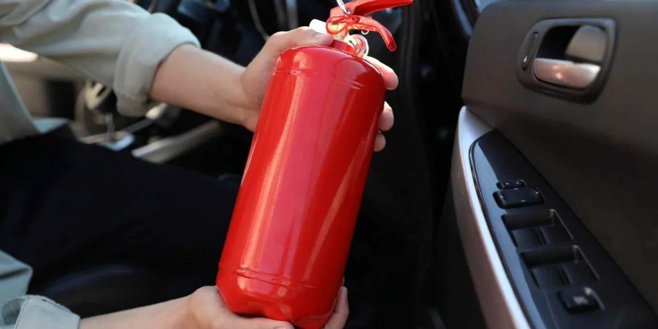 Ręce trzymające czerwoną gaśnicę samochodową. Zastanawiasz się, co zrobić ze starą gaśnicą samochodową?