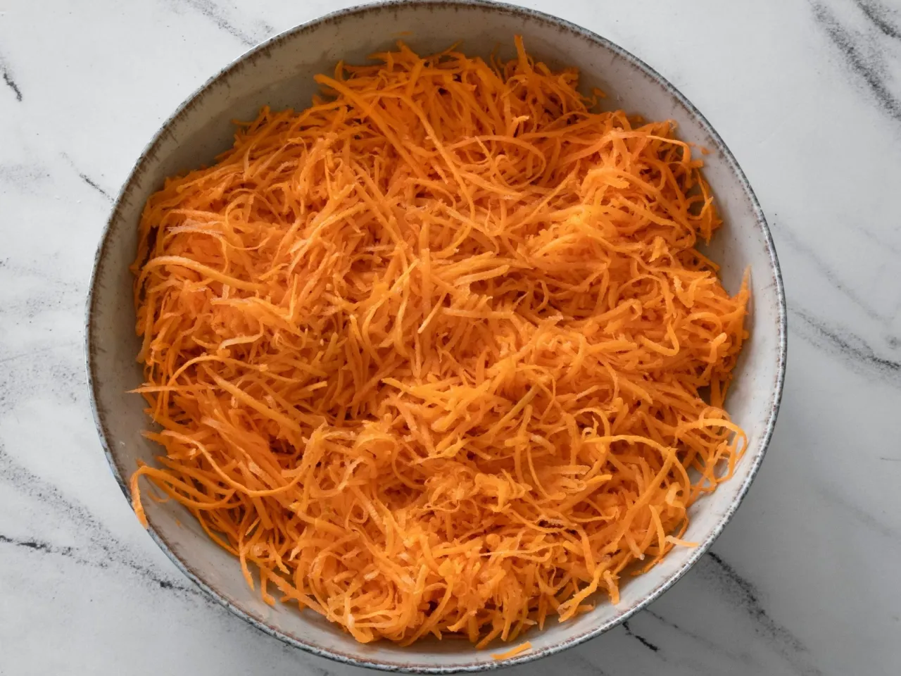 Miseczka pełna startej marchewki, gotowa na sur&oacute;wkę z marchewki jak z restauracji.