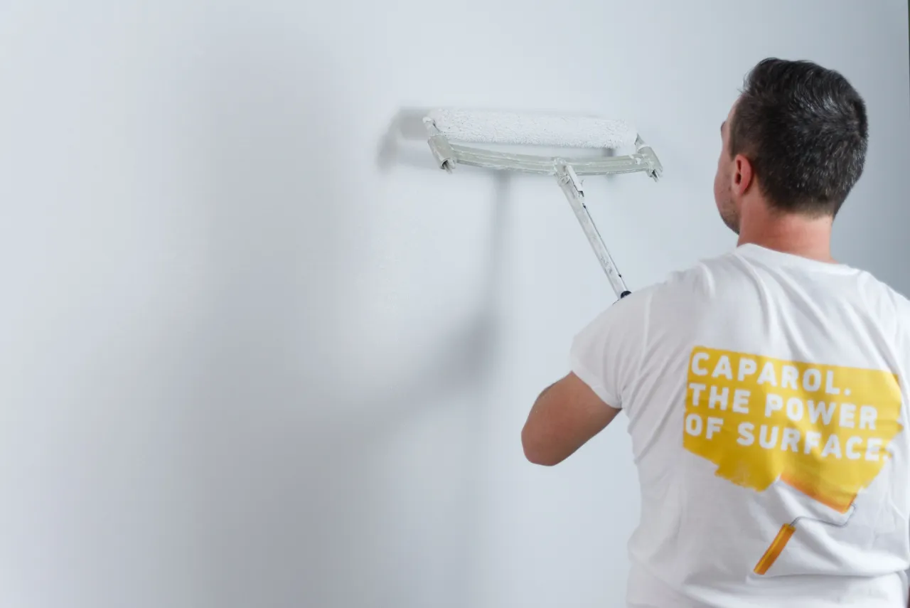 Mężczyzna maluje białą ścianę wałkiem. Zastanawiasz się, jak często malować mieszkanie? Odświeżenie wnętrza to dobry pomysł!