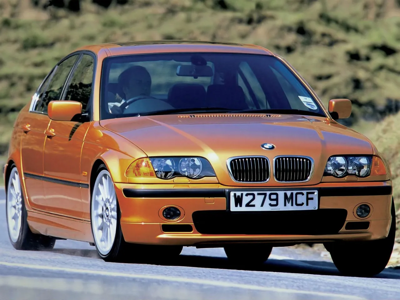 Pomarańczowe BMW E46, produkowane w latach 1997-2006, pędzi po drodze.