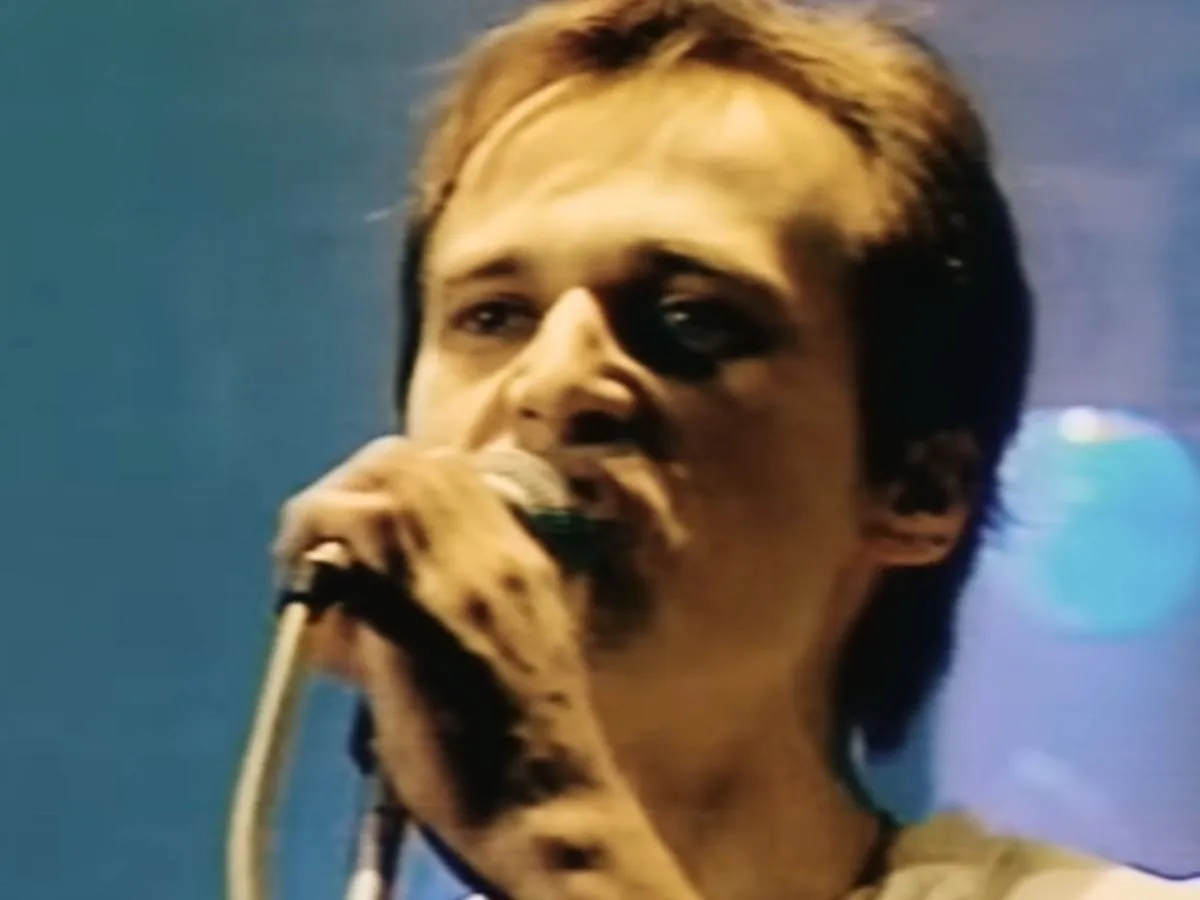 Mężczyzna z mikrofonem, jego aya rl sk&oacute;ra lśni w świetle. Kto śpiewa?