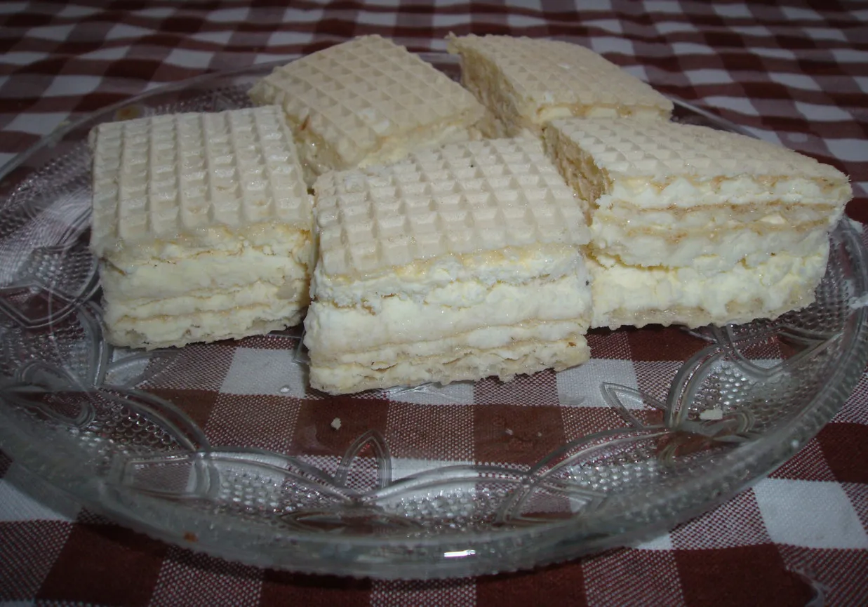 Sześć kwadratowych wafli przekładanych kremem, przypominających lody śnieżka prl, na szklanej paterze.