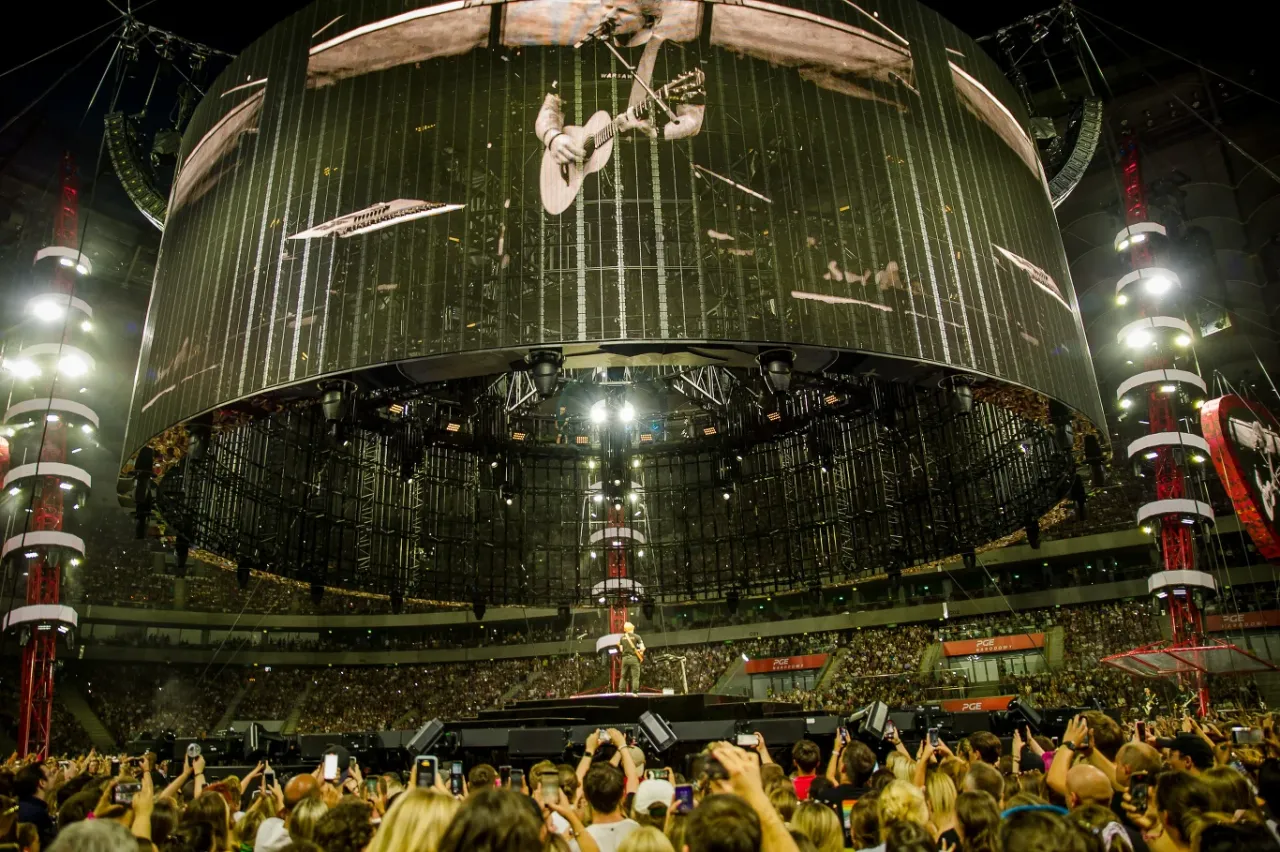 Ed Sheeran w Warszawie zgromadził tłumy. Ogromny ekran pokazuje artystę, a pod nim tysiące fan&oacute;w z telefonami.