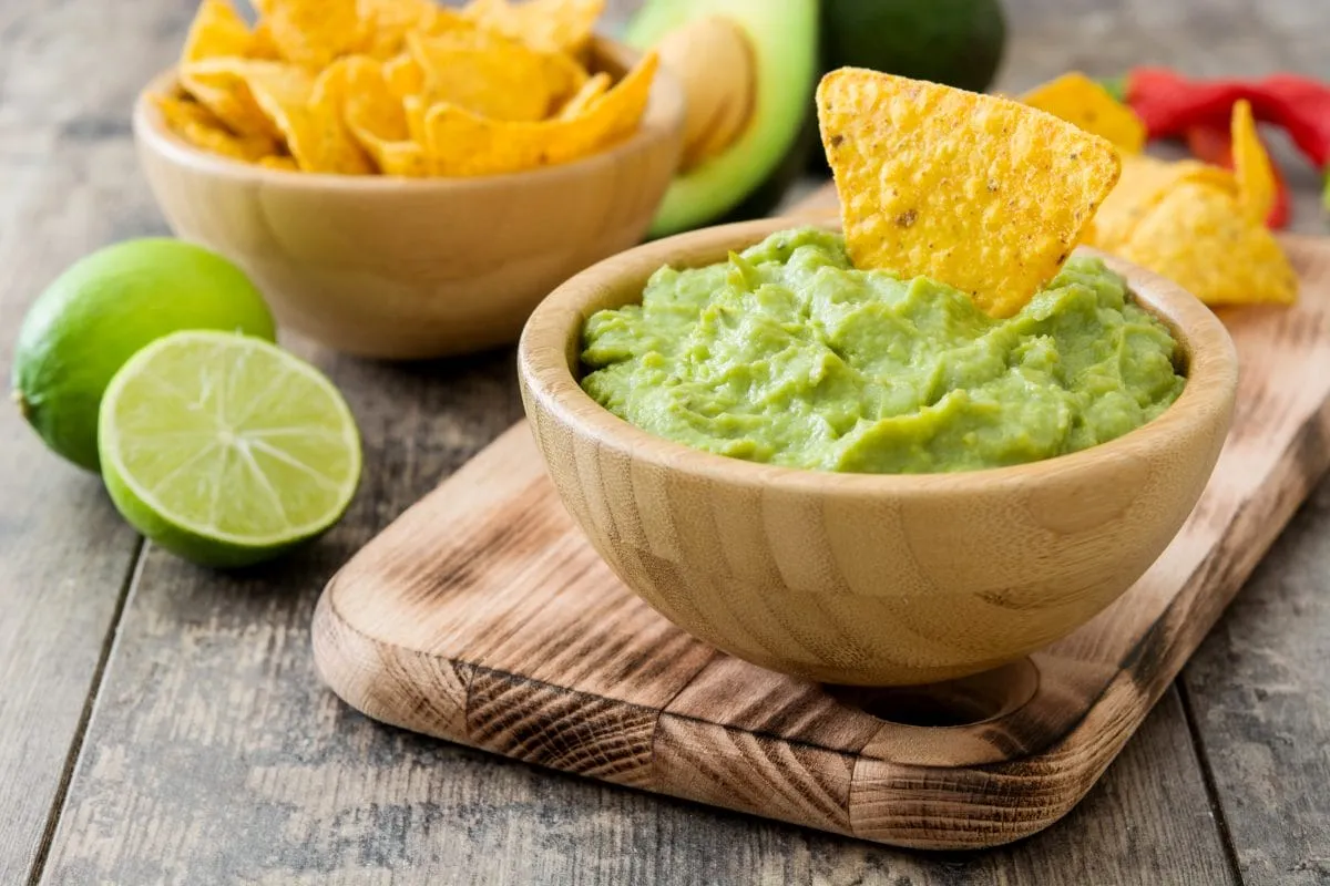 Miseczka guacamole z nachos i limonkami. Czy guacamole jest zdrowe? Tak, to pyszna i pełna zdrowych tłuszczów przekąska.