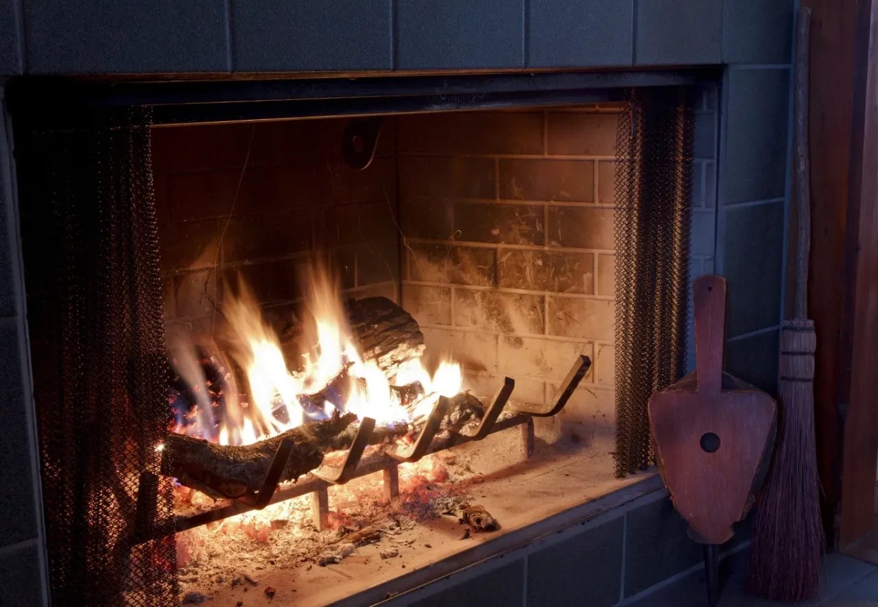 Płonące drewno w kominku, obok miotła i miech. Idealne na chłodne wieczory, choć warto pamiętać, do kiedy można palić drewnem.