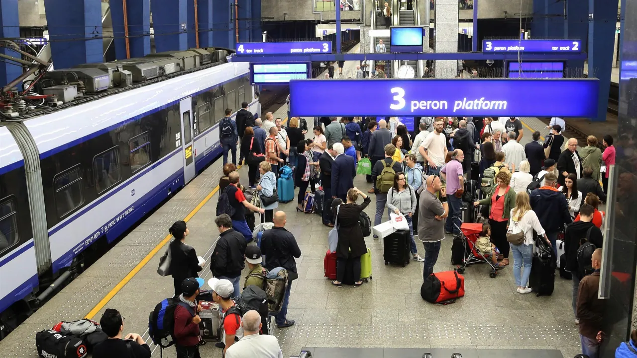 Tłum ludzi czeka na pociąg Intercity. Tablica informuje, z kt&oacute;rego peronu odjeżdża pociąg: peron 3.