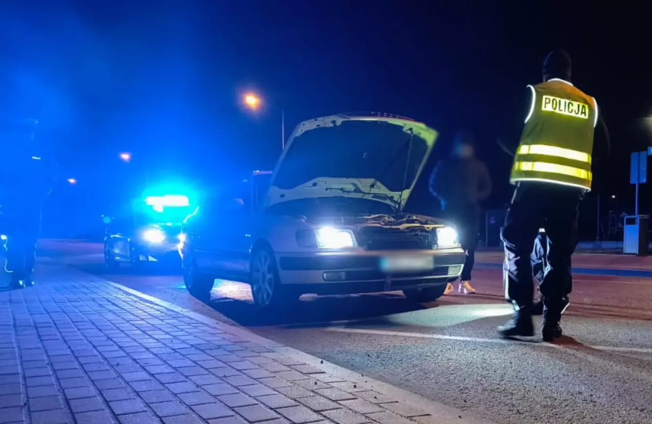 Policja przerwała nielegalne wyścigi. Samochód z otwartą maską, policyjne światła i funkcjonariusz w kamizelce odblaskowej.