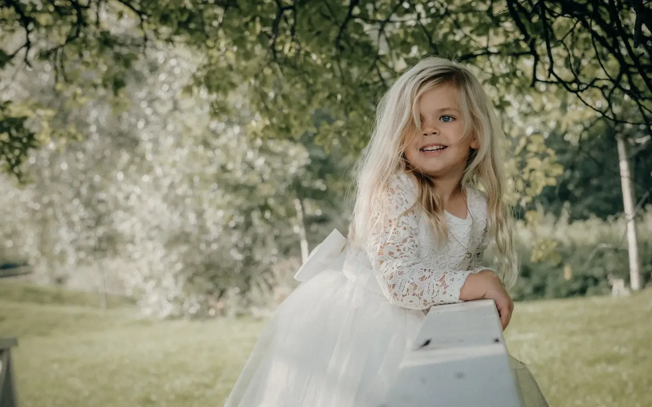Uśmiechnięta dziewczynka w białej sukience z koronkowymi rękawami. Czy na komunie można ubrać się na biało? Tak, wygląda uroczo!