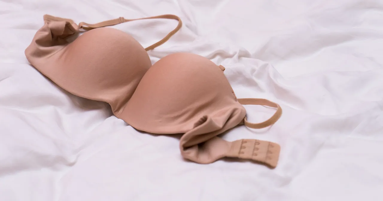 Beżowy biustonosz z fiszbiną leży na białej pościeli.