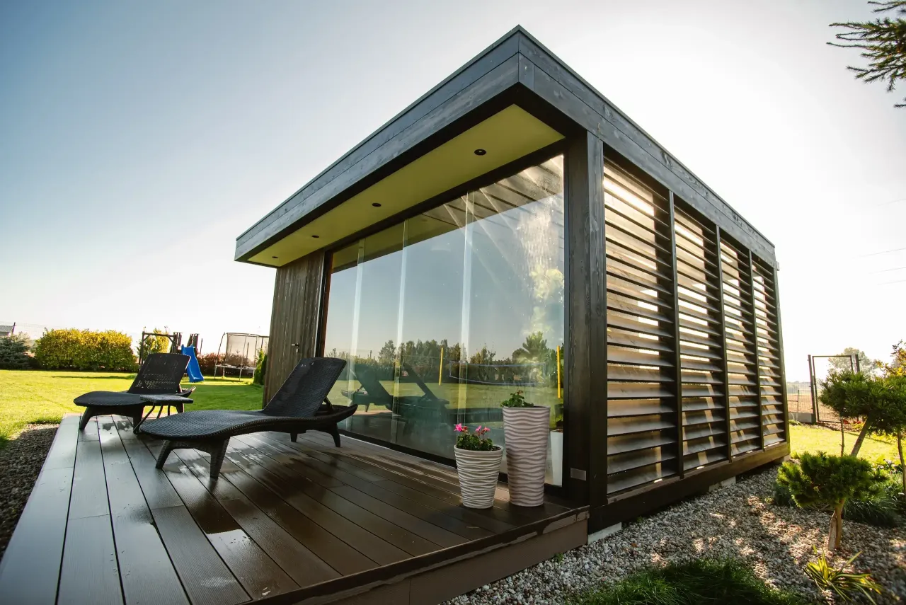 Nowoczesna altana z drewnianymi żaluzjami i przeszkloną ścianą. Idealne rozwiązanie, z czego zrobić ściany altany, by uzyskać stylowy wygląd i prywatność.