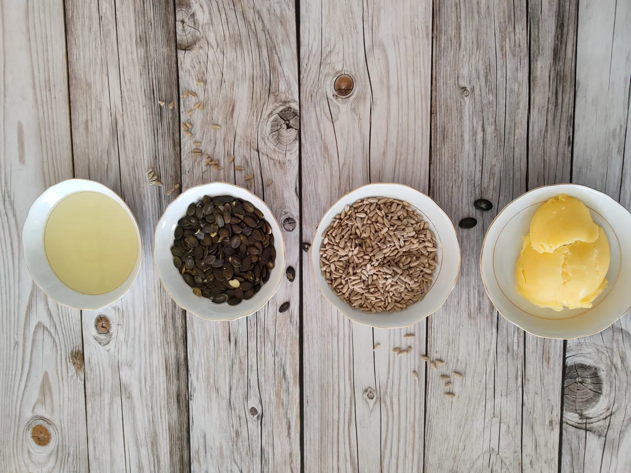 Cztery miseczki: olej, pestki dyni, słonecznik i masło. Porównanie tłuszcze roślinne czy zwierzęce.