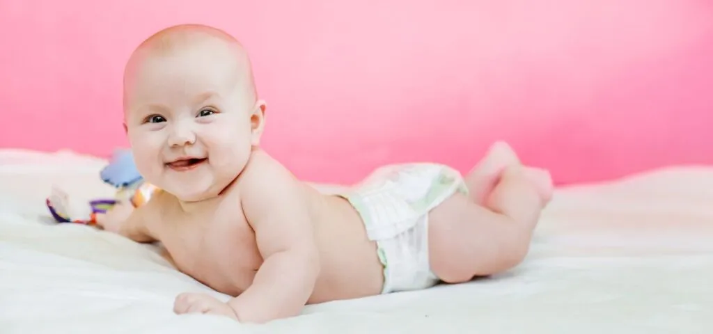 niemowlę leżące na brzuchu podnosi główkę i chwyta zabawkę
