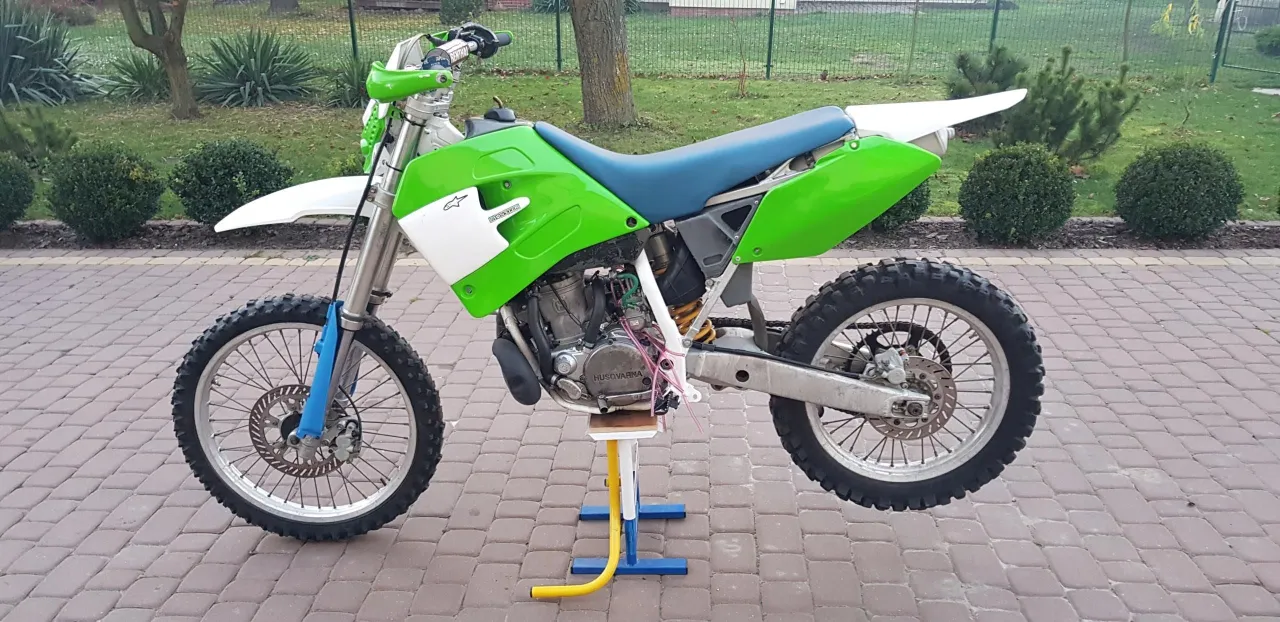 Zielony motocykl Husqvarna WR 250 na stojaku, gotowy do jazdy po wyboistym terenie.