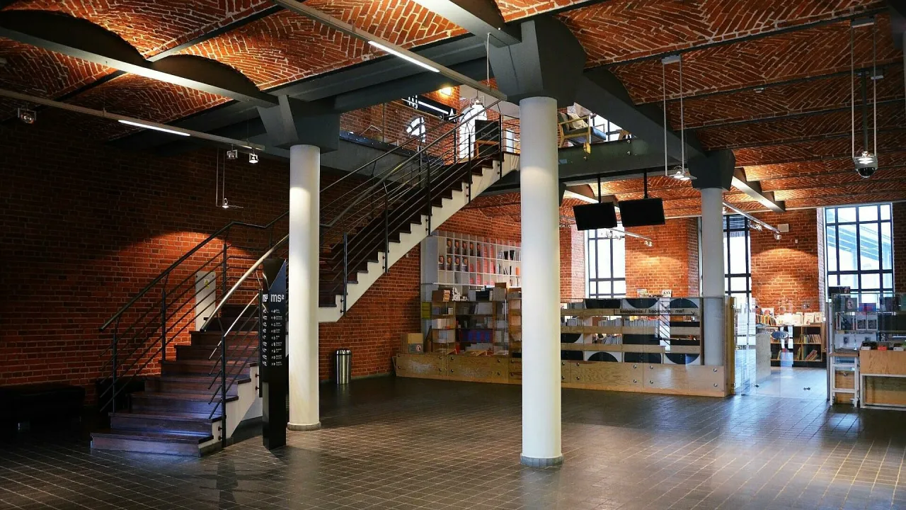 Wnętrze muzeum sztuki w Łodzi MS2. Ceglane ściany i sklepienia, nowoczesne schody, regały z książkami i ekspozycjami.