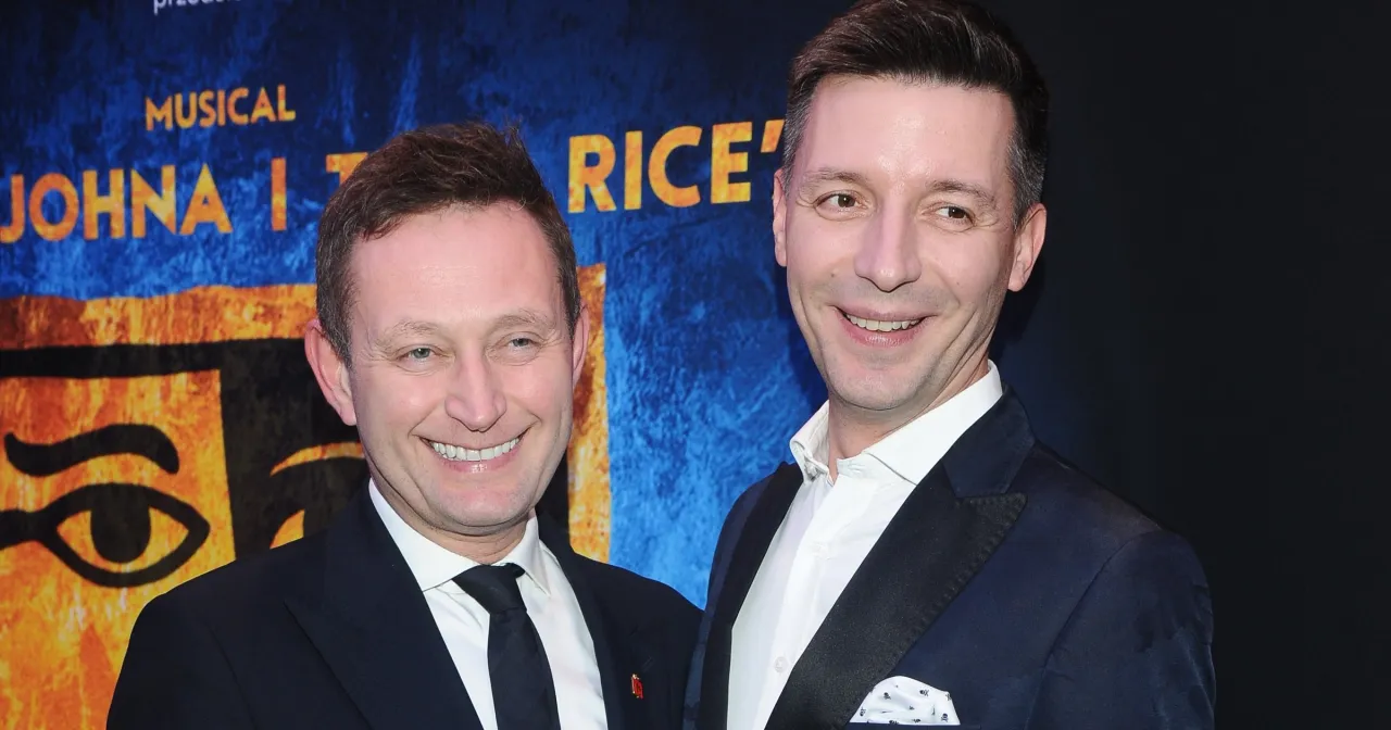 Dwóch mężczyzn pozuje do zdjęcia na tle plakatu musicalu. Jeden z nich, Michał Cessanis, uśmiecha się szeroko.