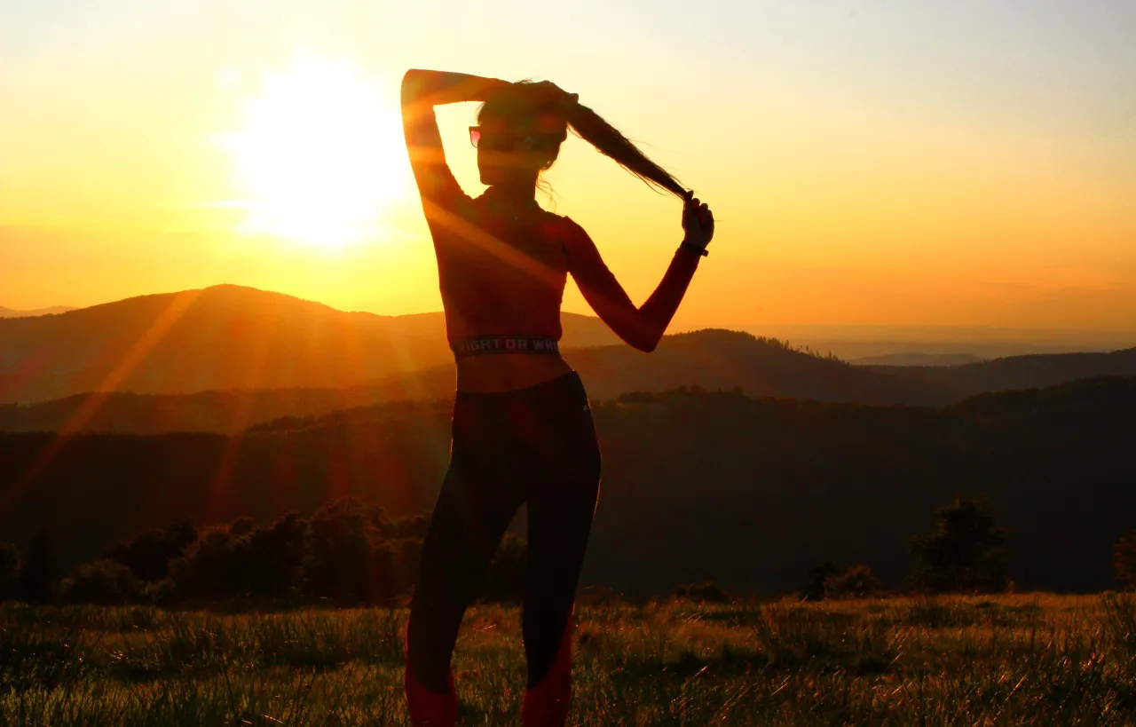 Osoba spacerująca po parku z uśmiechem, w tle zachód słońca