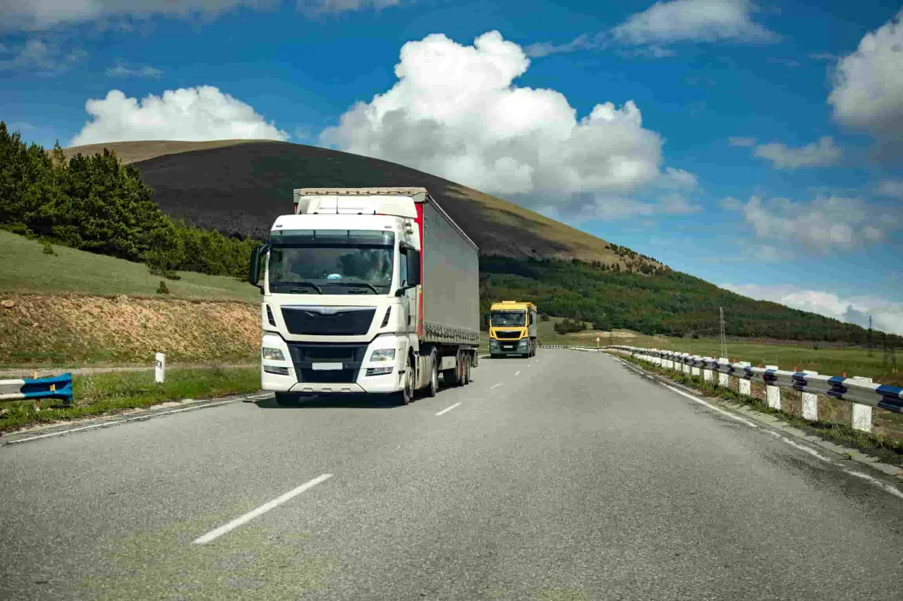 Dwie ciężar&oacute;wki jadące drogą w g&oacute;rskim krajobrazie. Myślisz o tym, jak założyć firmę transportową?
