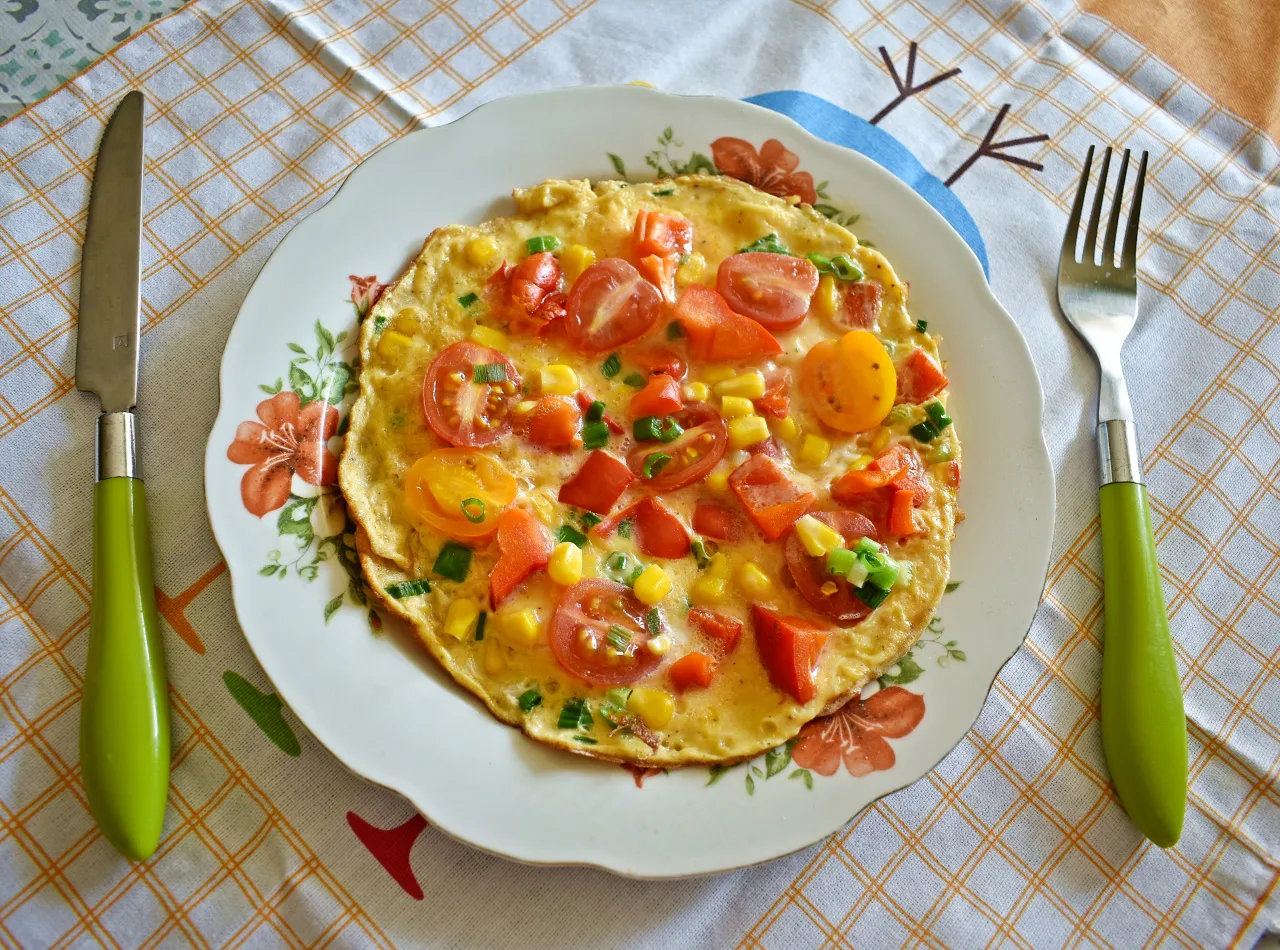 Kolorowy omlet z pomidorkami, kukurydzą i szczypiorkiem na talerzu. Idealny przykład, jak się robi omlet dietetyczny.