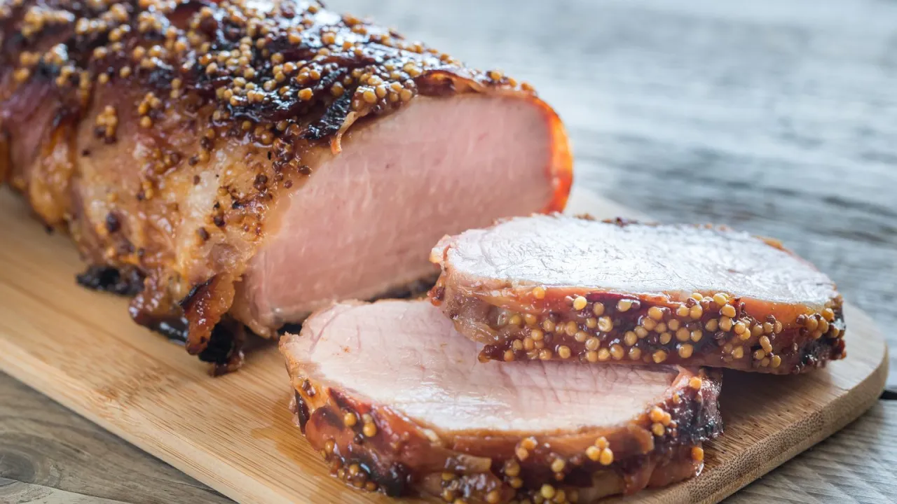 Pyszny, pieczony schab z musztardą i ziołami, pokrojony w plastry na desce.