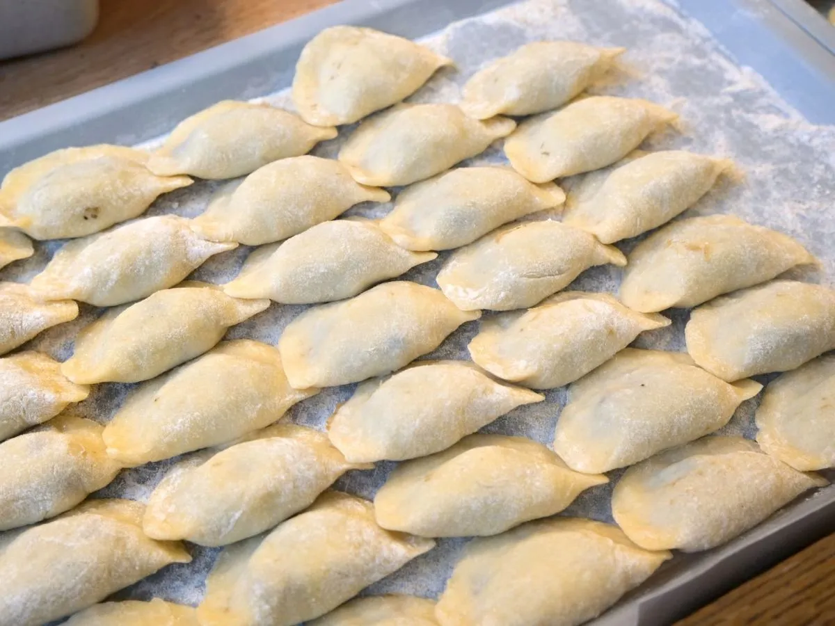 Ułożone na tacy surowe pierogi, gotowe do przechowywania w lodówce.