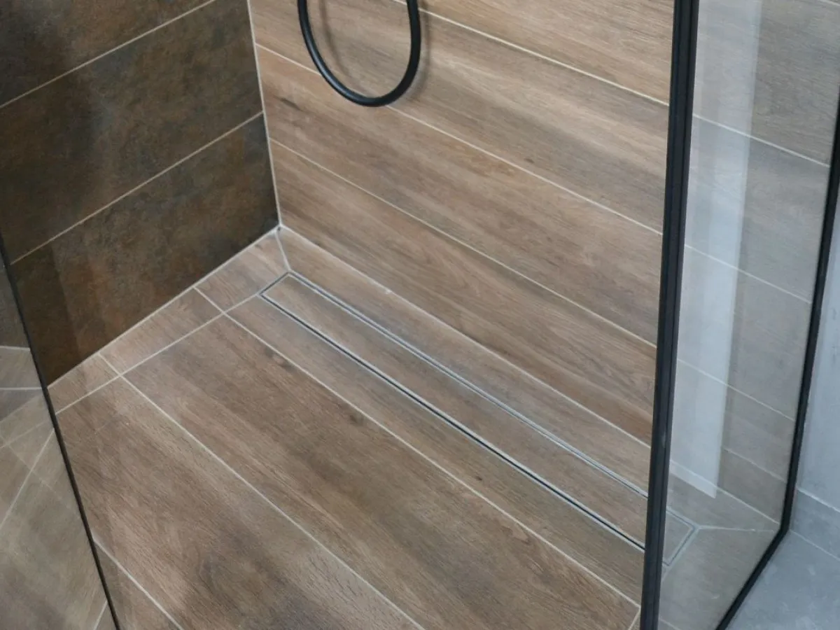 Nowoczesna łazienka z odpływem liniowym. Wylewka pod odpływ liniowy wykonana z płytek imitujących drewno.