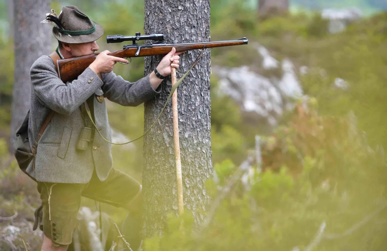 Myśliwy w tradycyjnym stroju celuje z karabinu. Czy myśliwi zarabiają na swojej pasji?
