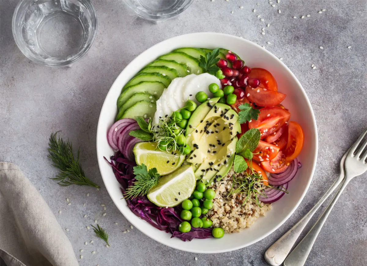 Kolorowa buddha bowl z awokado, pomidorami, og&oacute;rkiem, czerwoną cebulą, groszkiem, granatem i komosą ryżową.