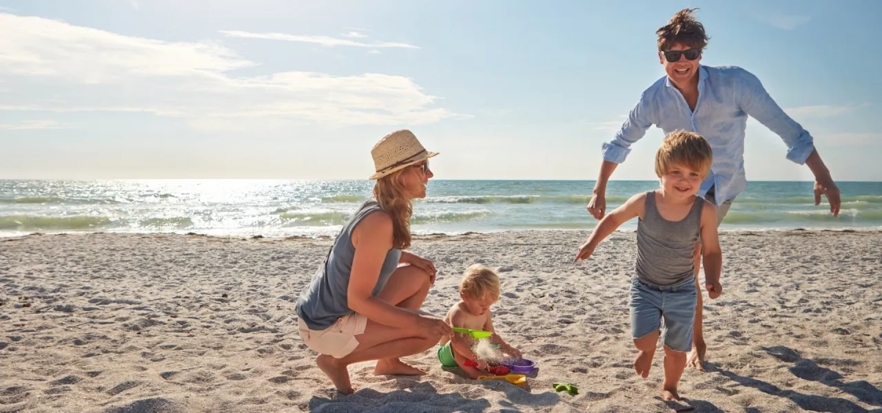 Rodzinne wakacje z dzieckiem nad morzem. Uśmiechnięta rodzina bawi się na plaży, budując zamki z piasku.