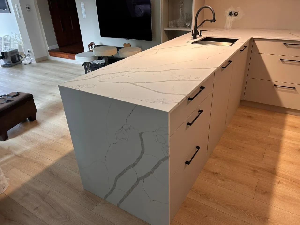 Nowoczesna kuchnia z wyspą z konglomeratu kwarcowego w Poznaniu. Jasny blat z żyłkowanym wzorem, czarny zlew i bateria.