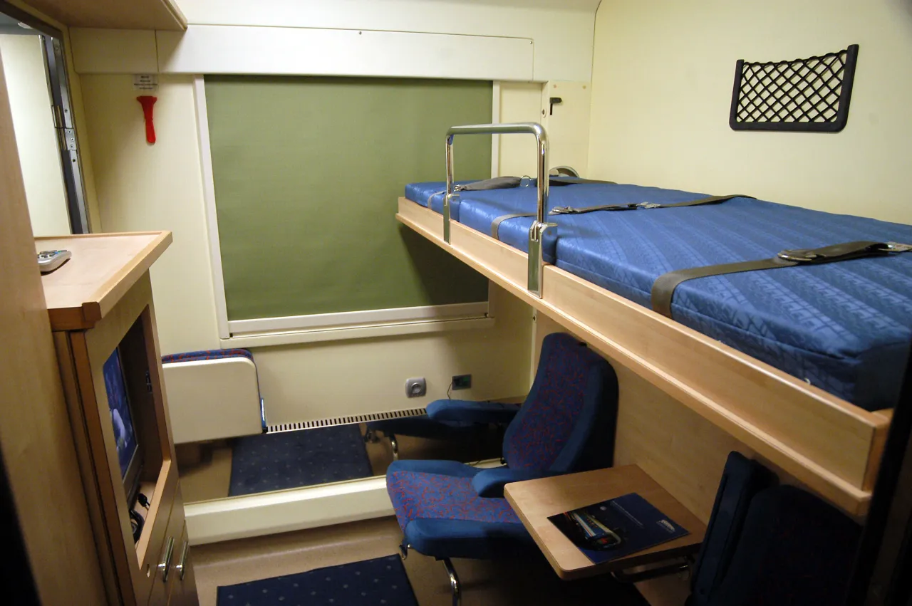 Wnętrze wagonu sypialnego z łóżkiem, siedzeniami i stolikiem. Zastanawiasz się, ile kosztuje wagon sypialny?