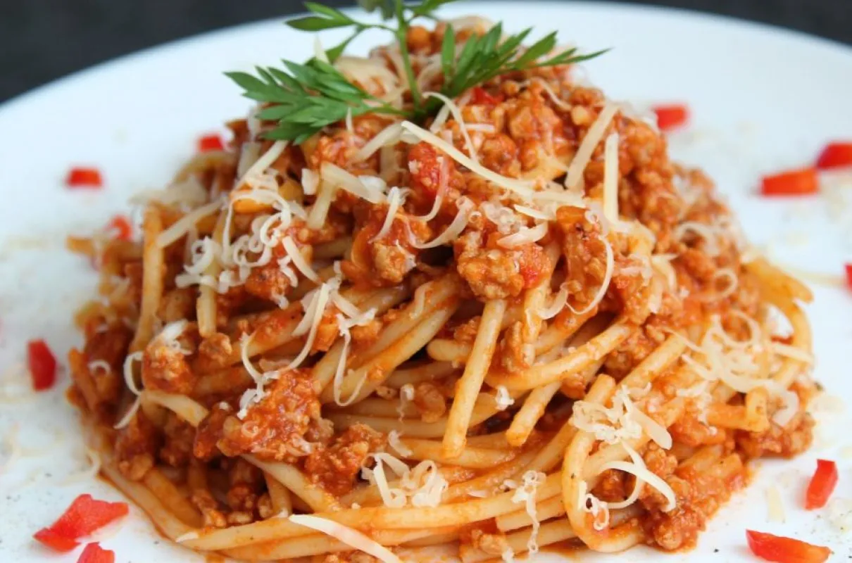 Pyszne spaghetti z sosem bolognese, posypane parmezanem i udekorowane natką pietruszki. Idealne pytanie: co zrobic z sosem bolognese?
