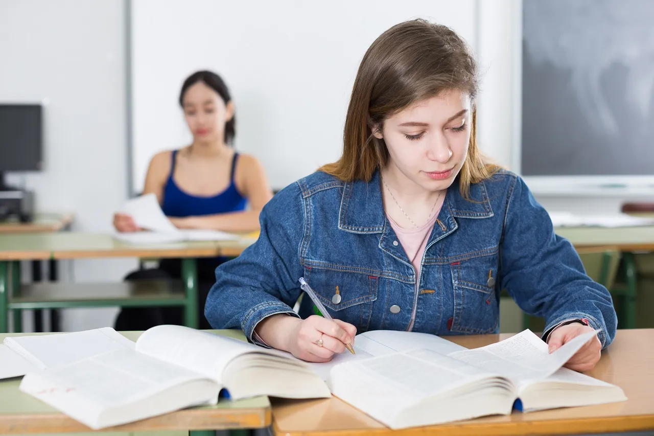 uczeń piszący wypracowanie przy biurku z książkami